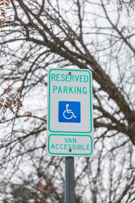 The image features a reserved parking sign with a blue wheelchair access symbol, indicating accessibility for disabled parking and van access. The sign is mounted on a silver pole against a background