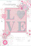 This anniversary card carries an air of soft refinement, the kind of timeless romance that suits Marylebone's calm streets and leafy squares. Central to the design is the word LOVE, rendered in raised, generously glittered letters that blend blush pink, pearly white, and silver shimmer. The glitter is delicately applied, giving the letters a frosted, almost velvety appearance that invites touch. They stand against a smooth blush-pink background, subtly luminous, like the gentle glow of early evening light over nearby Regent's Park. Flowing around this central motif, a pattern of stylised flowers and twining leaves drifts across the card's surface. The blossoms appear in soft pastel tones, their outlines fine and graceful, as though sketched by a florist planning a romantic bouquet with layered petals and trailing greenery. Silver accents trace the edges of selected petals and spiralling vines, catching light in a sophisticated glimmer that adds depth and movement. The floral design grows denser near the word LOVE and then eases into lighter sprays, creating a sense of balance and quiet motion. An anniversary message in an elegant script, expressing continuing love and devotion, sits in harmony with the decorative elements, its looping letters mirroring the curves of the foliage. The card's gentle embossing around the letters and flowers adds a tactile richness, making it feel like a keepsake rather than a simple greeting. Overall, it evokes a sense of enduring affection and shared life-an ideal companion to a bouquet delivered in Marylebone for a heartfelt anniversary celebration.
